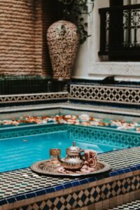 The courtyard of a beautiful riad with a pool and lush greenery Elegant Moroccan tea setting by a vibrant pool with intricate tile designs in Marrakesh.