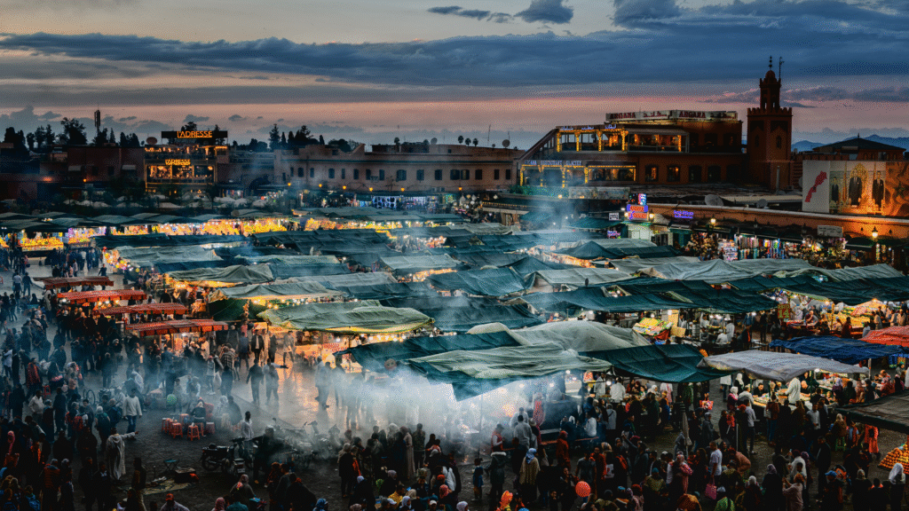 A wide shot of Jemaa el-Fna square at dusk/night, vibrant with lights and activity, Jemaa el-Fna square in Marrakech at night Vibrant evening scene in Marrakech's main square